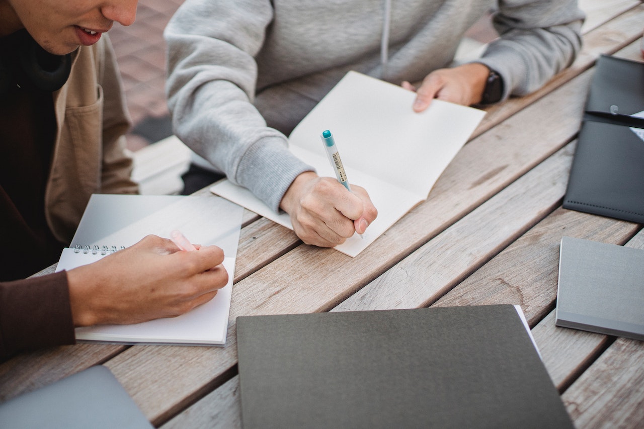 Crop unrecognizable male students writing essay in park